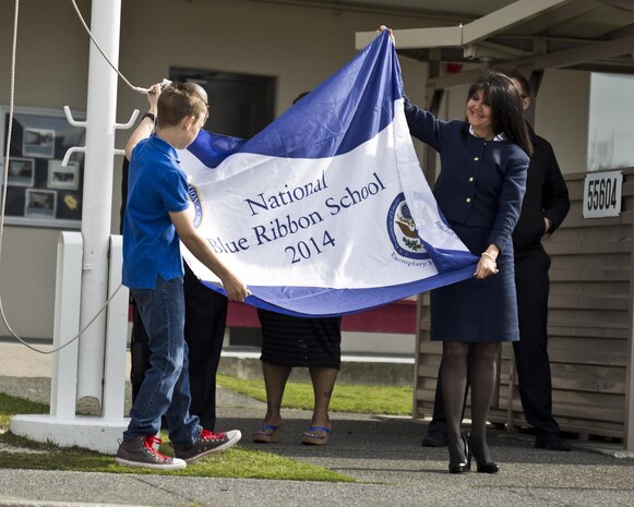 Suzanne Landrum, principal of M. C. Perry Elementary, assists a student in the raising of their Blue Ribbon School of Excellence flag during their Blue Ribbon ceremony aboard Marine Corps Air Station Iwakuni, Japan, April 21, 2015. The Department of Defense Education Activity nominates only three schools for the Blue Ribbon Schools of Excellence award annually, one from DoD Dependent School’s Europe, one from DoDEA Pacific and one from Domestic Dependent Elementary and Secondary Schools and this year M. C. Perry was selected along with Aukamm Elementary School in Germany.