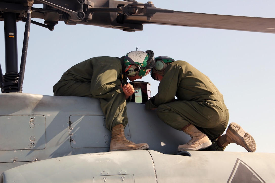 Aircraft mechanic Marines with Marine Aviation Weapons and Tactics Squadron 1 inspect the top of an AH-1W Super Cobra helicopter during a routine maintenance inspection during Weapons and Tactics Instructor course 2-15 aboard Marine Corps Air Station Yuma, Arizona, April 22, 2015. The maintenance that they provide ensures all pilot candidates complete every mission safely. WTI is a seven-week course hosted by MAWTS-1 that provides advanced tactical training to certify Marine pilots as weapons and tactics instructors, preparing them to return to the fleet and serve in key training officer billets. (U.S. Marine Corps photo by Sgt. Cody Haas)