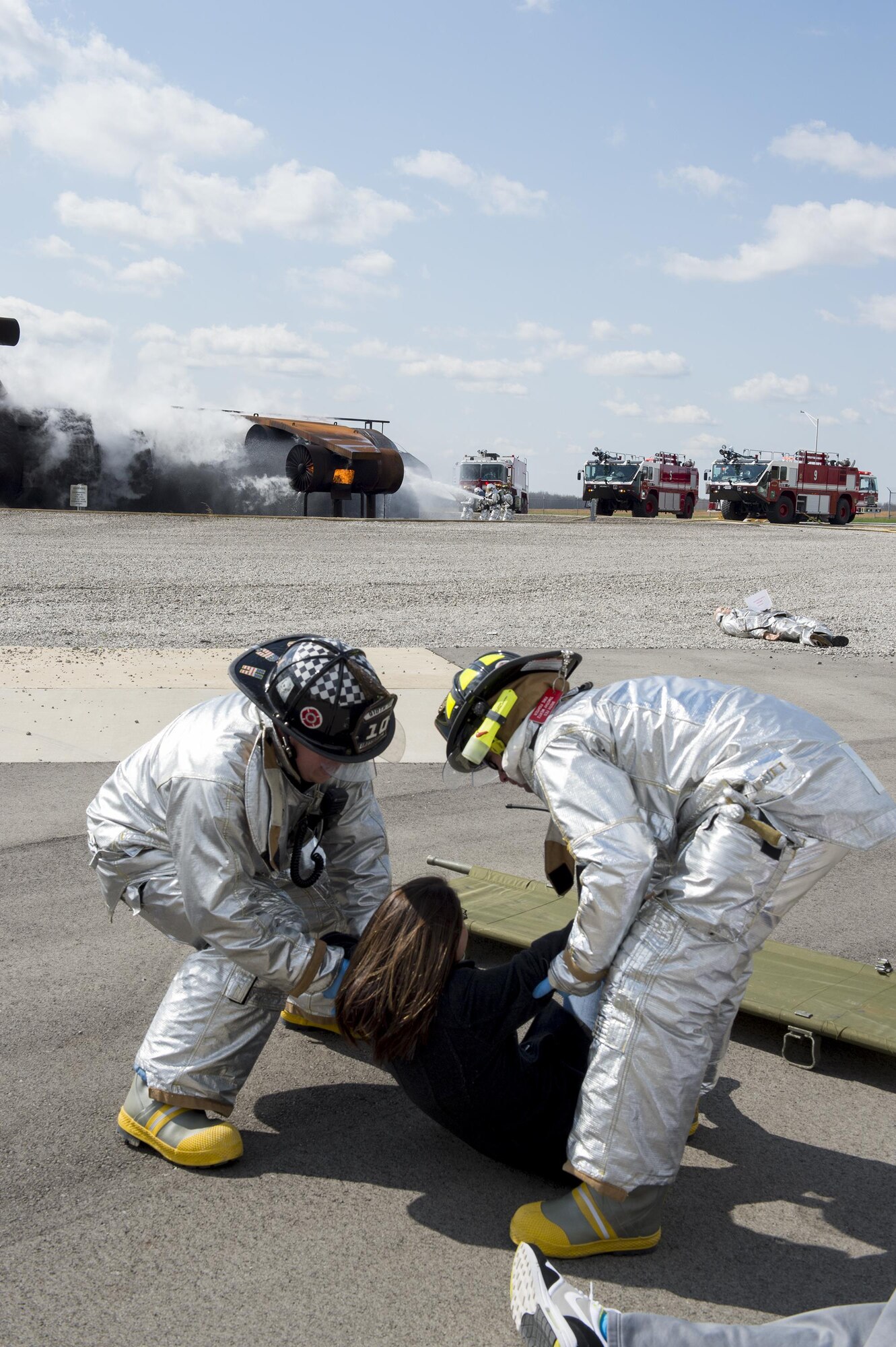 Tim Wertz and Christ Kail, firefighters with the 910th Civil Engineer Squadron fire department here, assist a victim during a multi-agency anti-hijacking exercise held here, April 24, 2015. In the background, other 910th firefighters fight a blaze on a training aircraft, simulating a commercial aircraft after terrorists detonate and explosive device. Participating agencies included the Western Reserve Port Authority, Youngstown-Warren Regional Airport, local law enforcement and fire departments, the Federal Bureau of Investigation, the Federal Aviation Administration and Air Force Reserve. (U.S. Air Force photo/Eric M. White)  