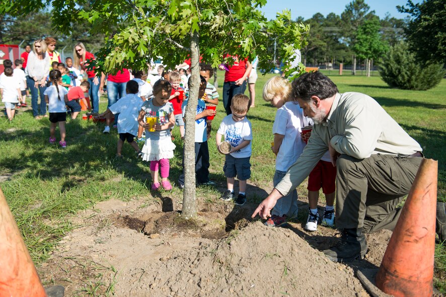 John Crain, 23d Civil Engineer Squadron forester, helps children plant a nuttall oak tree during an Arbor Day tree planting ceremony April 24, 2015, at Moody Air Force Base, Ga. For every year since 1999, Moody has planted a new tree in its Tree City USA Park. (U.S. Air Force photo by Airman 1st Class Dillian Bamman/Released)
