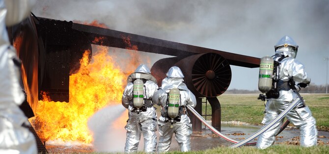 Firefighters of the 509th Civil Engineer Squadron execute coordinated movements and use teamwork to extinguish flames during a fire pit training exercise at Whiteman Air Force Base, Mo. April 2, 2015. The exercise uses controlled burns to simulate conditions of a real-world crash site. (U.S. Air Force photo by Airman 1st Class Jovan Banks/Released)
