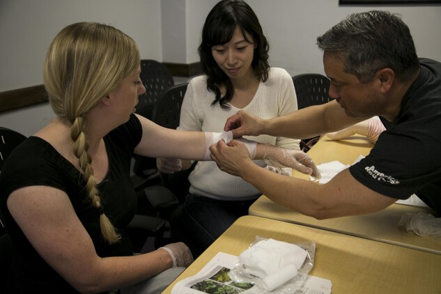 Hailey J. Day, right, Kaori Miyanishi, center, and Allen Balabis, practice wrapping a simulated wound during a class sponsored by the American Red Cross in the education center April 22 on Camp Foster, Okinawa. The class certified Marines and Master Labor Contractors in adult, child and infant CPR, use of an automated external defibrillator and basic first aid. Day is a financial official with G-6 communications, Marine Corps Installations Pacific-Marine Corps Base Camp Butler, Japan. Miyanishi is the community relations specialist with the Okinawa field office, U.S. Forces Japan, Balabis is the regional director of emergency management for MCIPAC.