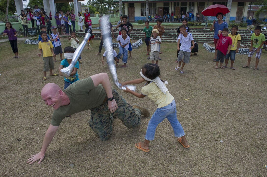 U.S. Marine Capt. Paul Brashier, a civil affairs Marine assigned to III Marine Expeditionary Force, gets whacked with improvised foam bats during a team building exercise at Don Joaquin Artuz Memorial Elementary School in Tapaz, Philippines, during Balikatan 2015, April 23. Brashier, a member of the Combined-Joint Civil-Military Operations Task Force on the island of Panay, took advantage of some time before a mural painting project at the school to entertain the children. Balikatan, which means “shoulder to shoulder” in Filipino, is an annual bilateral training exercise aimed at improving the ability of Philippine and U.S. military forces to work together during planning, humanitarian assistance
and disaster relief operations. (U.S. Navy photo by Chief Mass Communication Specialist Lowell
Whitman/Released)