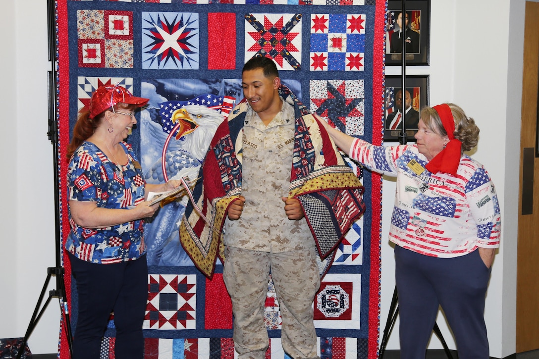 Cpl Adrian Velasco, administrative specialist aboard Marine Corps Logistics Base Barstow, is presented with a hand made quilt from the Quilts of Valor Foundation on Apr. 27.  Quilts of Valor recognizes service members like Velasco upon returning from deployments and presents them with patriotic quilts free of charge. 