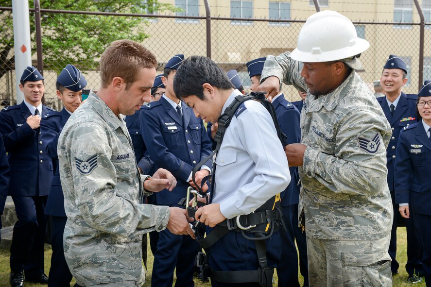 (Left to right) U.S. Air Force Staff Sgt. Zachary Aguiar and Staff Sgt. Sean Hicks, both with the 374th Communications Squadron cable and antenna system shop, assists a Japan Air Self-Defense Force communications officer student in dawning a safety harness during a communication site visit at Yokota Air Base, Japan, April 24, 2015.  The JASDF students are from the 4th Technical School, Kumagaya Air Base. (U.S. Air Force photo by Senior Airman Desiree Economides/Released)