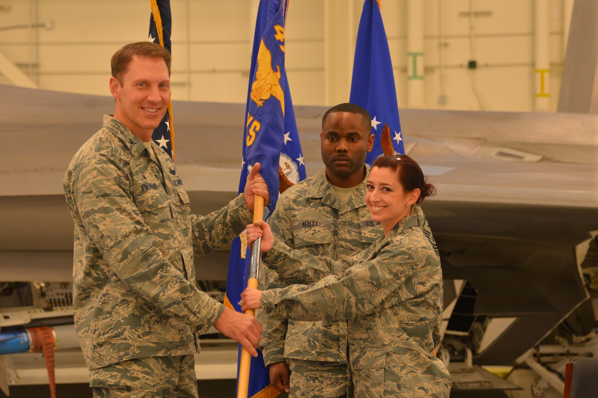 Col. David Piffarerio, 477th Fighter Group Commander, presents the 477th Aircraft Maintenance Squadron colors to Maj. Jessica Pisano, the new 477th AMXS Commander, during a change of command ceremony held here April 12, 2015.(US Air Force photo/Tech. Sgt. Dana Rosso)