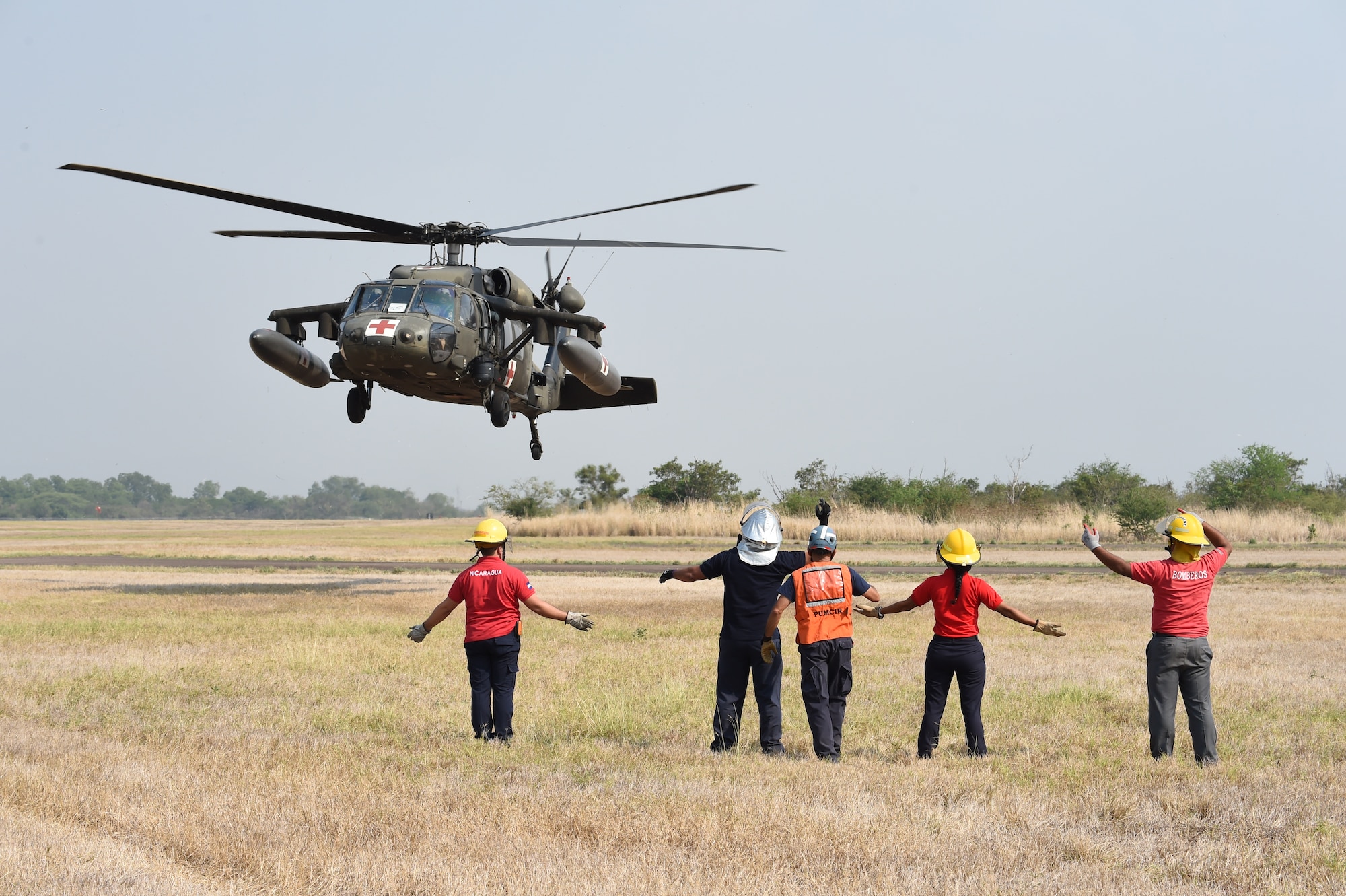 Firefighters hail an HH-60 Blackhawk as part of a simulated emergency rescue operation April 23, 2015, at Soto Cano Air Base, Honduras. The simulated rescue was part of the Central America Sharing Mutual Operations Knowledge and Experience exercise, designed to build partnership capabilities by bring firefighters from the U.S. and Central American countries together as a unified team. (Photo by Martin Chahin)