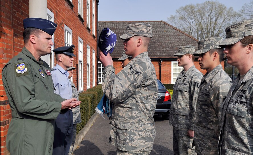 RAF Mildenhall base honor guard Airmen pass the American Flag to U.S. Air Force Col. Kenneth T. Bibb, Jr., 100th Air Refueling Wing commander, during the monthly retreat ceremony April 24, 2015, on RAF Mildenhall, England. In the time-honored tradition of the retreat ceremony, the U.S. flag and Royal Air Force ensign are folded to signify the end of the duty day. (U.S. Air Force photo by Airman 1st Class Kyla Gifford/Released)