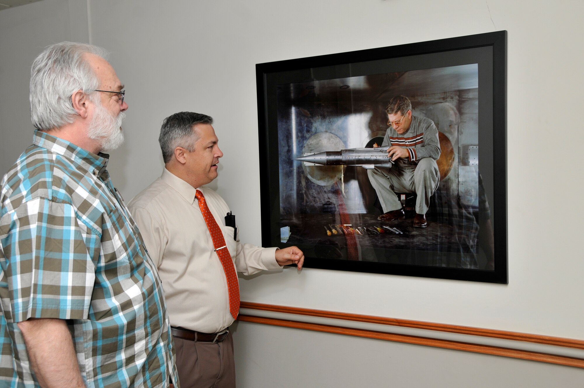 AEDC Photographer Rick Goodfriend (left) and AEDC Historian Chris Rumley view one of the prints recently mounted in the Administration and Engineering (A&E) building first floor hallway. Rumley coordinated the display of 50 AEDC photographs and drawings depicting AEDC history with the help of Goodfriend. Rumley plans to display 50 additional prints. (Photo by Jacqueline Cowan)