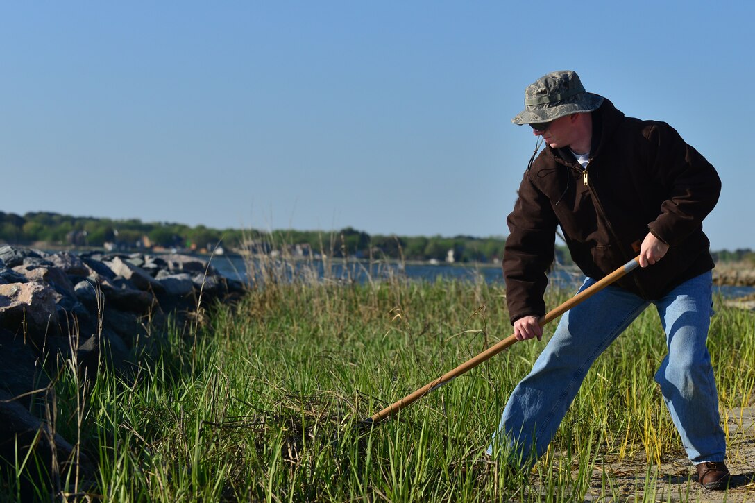 U.S. Air Force Staff Sgt. Carl Slater, 1st Maintenance Squadron ammo supervisors, rakes dead vegetation from the shoreline as part of Earth Week at Langley Air Force Base, Va., April 24, 2015. Along with ridding the area of dead vegetation, Airmen also planted new marsh. The marsh prevents erosion, which protects the inland area. (U.S. Air Force photo by Staff Sgt. Natasha Stannard/Released)