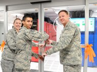 (Right to left) Air Force District of Washington Commander Maj. Gen. Darryl Burke, Staff Sgt. Julian Smith, and Lt. Col. Pamella Zane cut a ribbon officially opening the Shared Computing Environment at Joint Base Andrews, Md., April 24, 2015. The SCE architecture at Joint Base Andrews will reduce the hardware footprint and increase the support capacity to from 75,000 users to more than 200,000 users along the Eastern United States. Rogers is the 844th Communications Group chief technology officer. Smith is the 744th Communications Squadron NCO in charge of the SCE. Zane is the 744th CS commander. (U.S. Air Force photo/Master Sgt. Tammie Moore)