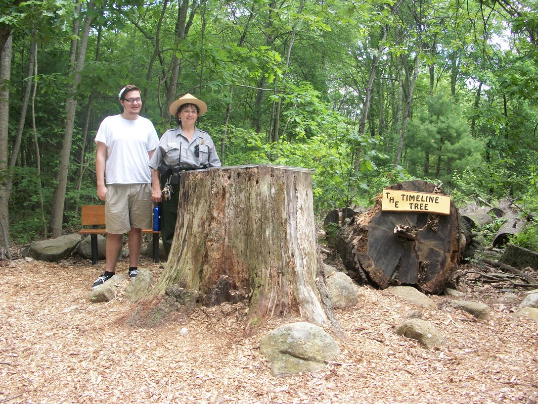 Boy Scout Brian DiPasquale and Park Ranger Viola Bramel stand at his Timeline Tree and bench project at the entrance of West Hill Dam, Uxbridge, Massachusetts.