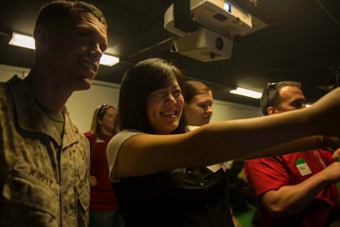 1st Lt. Evan Wimpey and his wife, Tian Wimpey, practice using a simulated M9 service pistol while participating in the II Marine Headquarters Group spouses event titled “In Their Boots,” more commonly known as Jane Wayne Day, aboard Camp Lejeune, N.C., April, 17, 2015. The event included hands-on practice at the Indoor Simulated Marksmanship Trainer and Combat Convoy Simulators, and aims to build cohesion and shed light on military training within the II MHG families. (U.S. Marine Corps photo by Lance Cpl. Fatmeh Saad/Released)