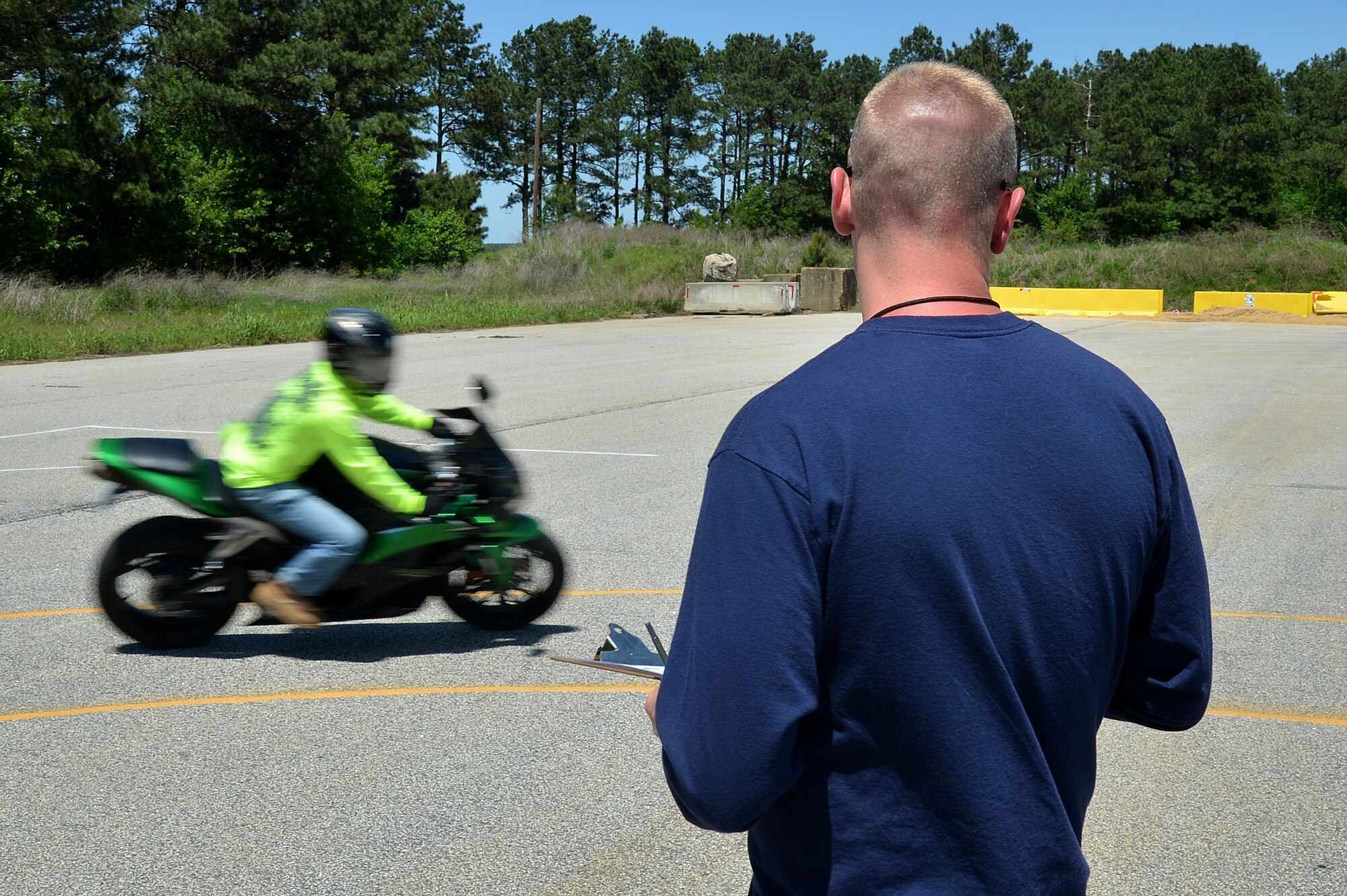 A student of the Rider Coach Preparation Workshop times a rider as he makes a turn at Shaw Air Force Base, S.C., April 22, 2015. The course was held to teach and certify Airmen and Soldiers as instructors of the Motorcycle Safety Foundation Basic Riders Courses One and Two.   (U.S. Air Force photo by Airman 1st Class Michael Cossaboom/Released)