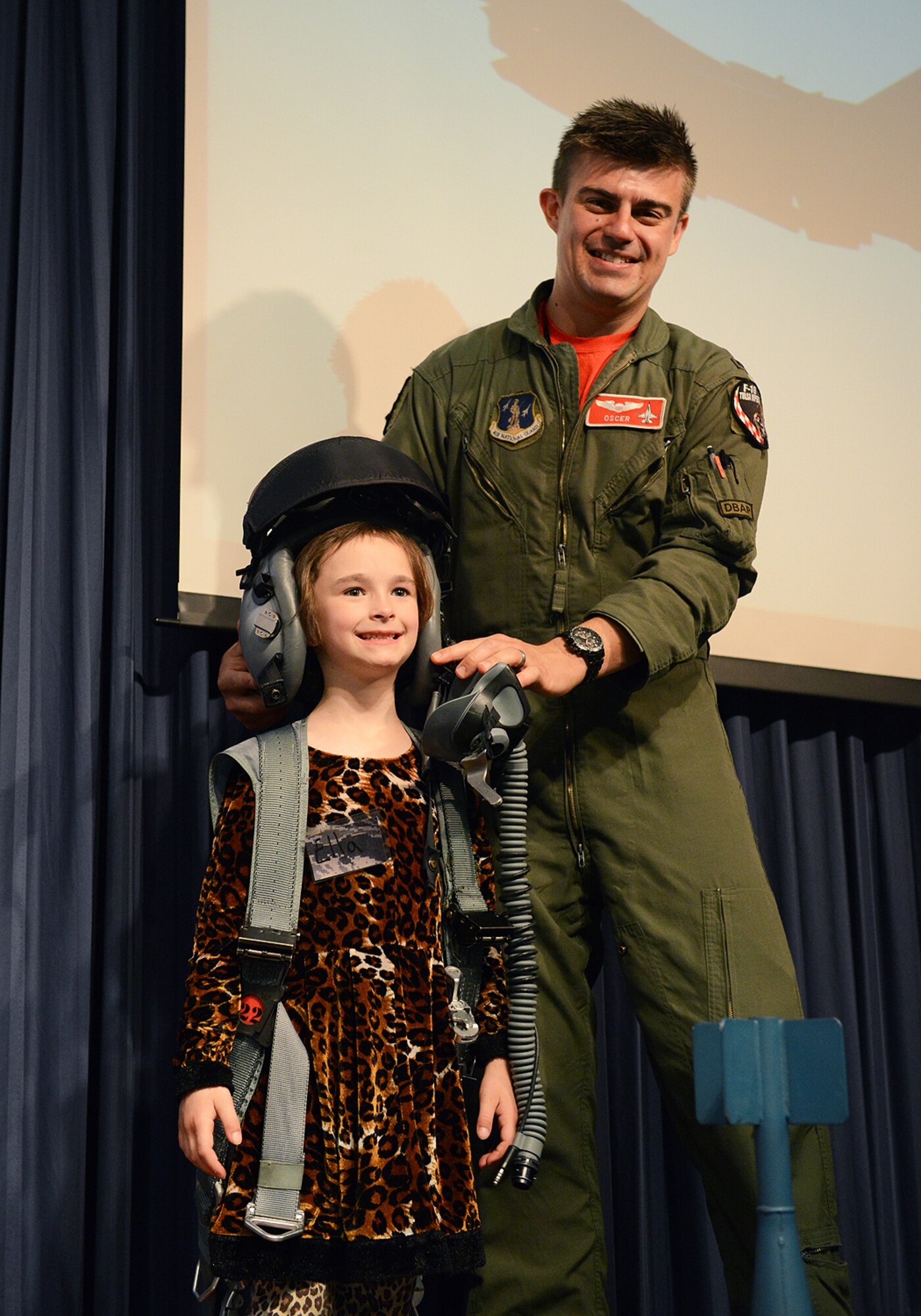 Ella Bennett, daughter of Tech. Sgt. Mason Bennett, 138th Logistics Readiness Squadron, tries on a flight helmet with the help of 1Lt. John Nowakowski, 125th Fighter Squadron at the Tulsa Air National Guard Base, Okla., 23 April, 2015, during "National Take Our Daughters and Sons to Work Day".   The 138th participated in the event as a way to give children an insight into what their parents do, as well as demonstrating to them what is involved day to day in a job or career.  (U.S. National Guard photo by Senior Master Sgt.  Preston L. Chasteen/Released)