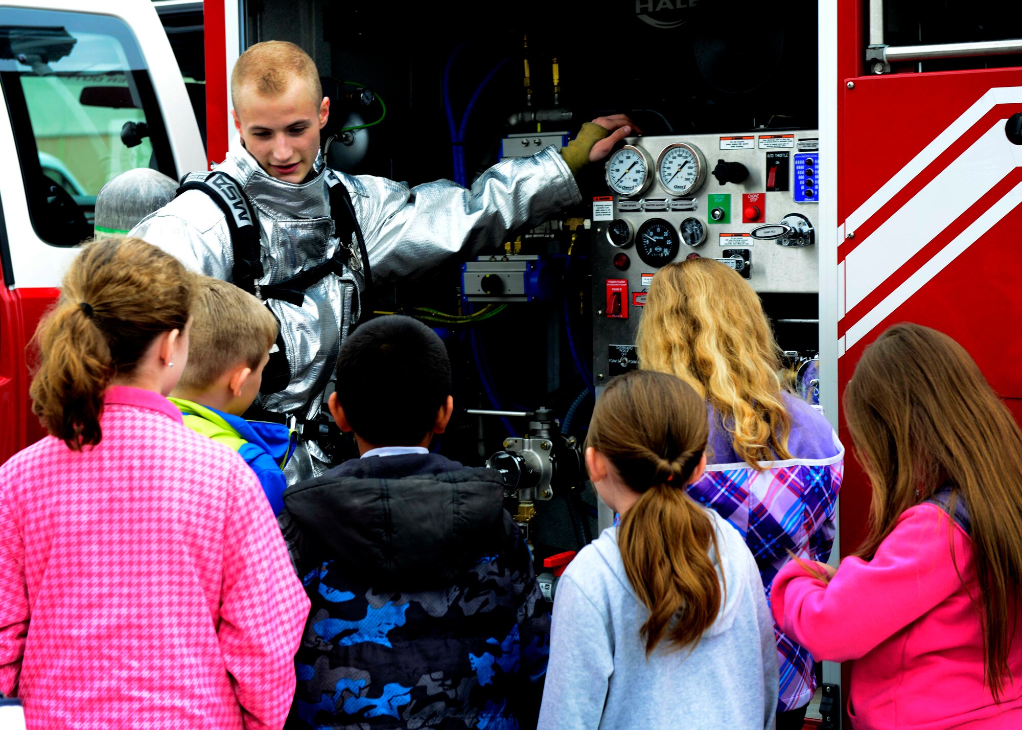 U.S. Air Force Airman 1st Class Joseph Cappel, 31st Civil Engineer Squadron firefighter, shows Aviano Middle/High School students fire truck equipment during a mock deployment, April 27, 2015, at Aviano Air Base, Italy. The event gave children a better understanding of what their parents do when deployed. (U.S. Air Photo by Senior Airman Areca T. Wilson/Released)