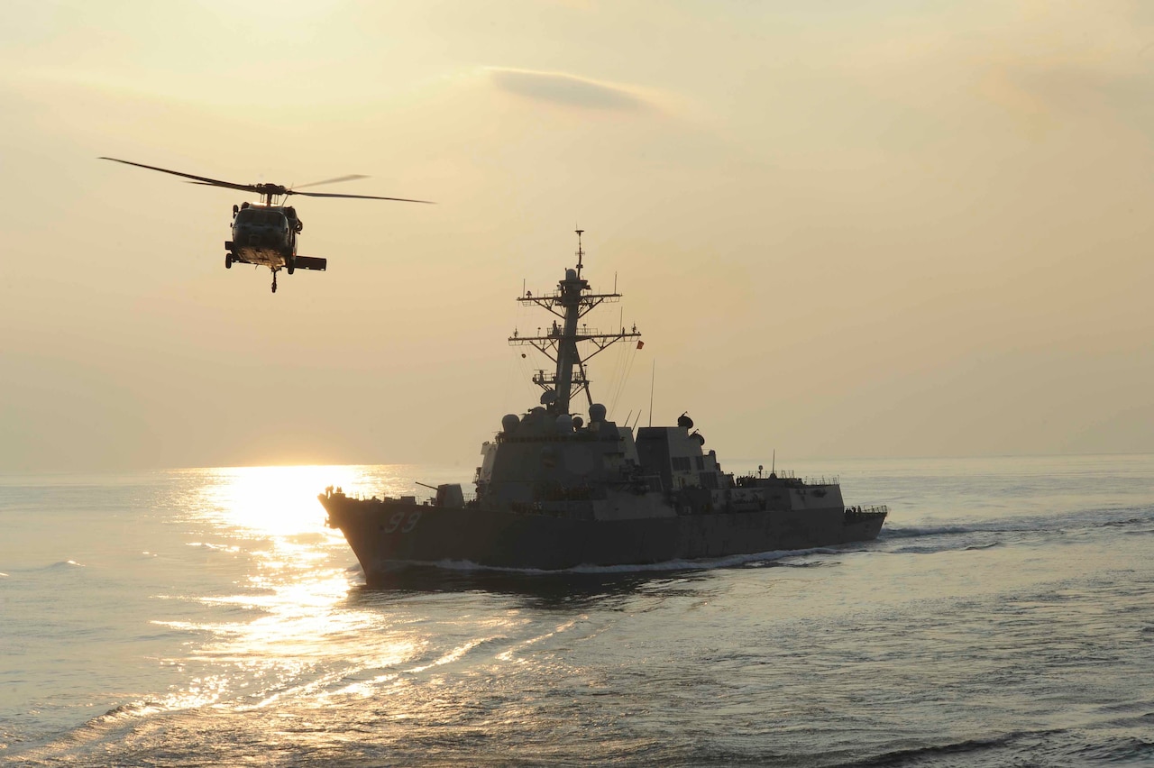 An MH-60S Knighthawk helicopter flies by the guided-missile destroyer USS Farragut during a replenishment-at-sea evolution in the Arabian Sea on Dec 4, 2012. U.S. Navy photo