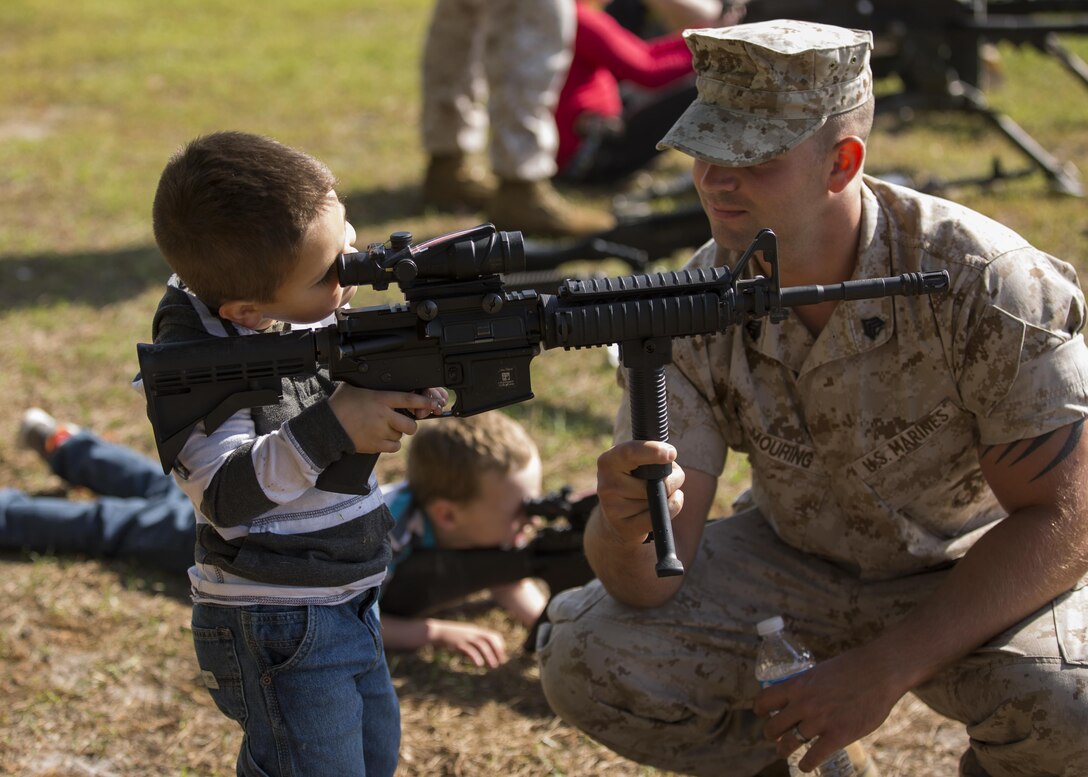 Sgt. Jesse Mouring, an electronic maintenance technician with 8th Communication Battalion, helps his son sight in with an M4 Carbine rifle during a "Bring Your Child To Work Day" aboard Camp Lejeune, N.C., April 23, 2015. This event brought Marines, sailors and their children together to see what their parents do on a day-to-day basis. The children ran through a modified combat fitness test, saw weapon systems and communications gear before ending the day with food and refreshments. (Lance Cpl. Olivia McDonald/ Released)