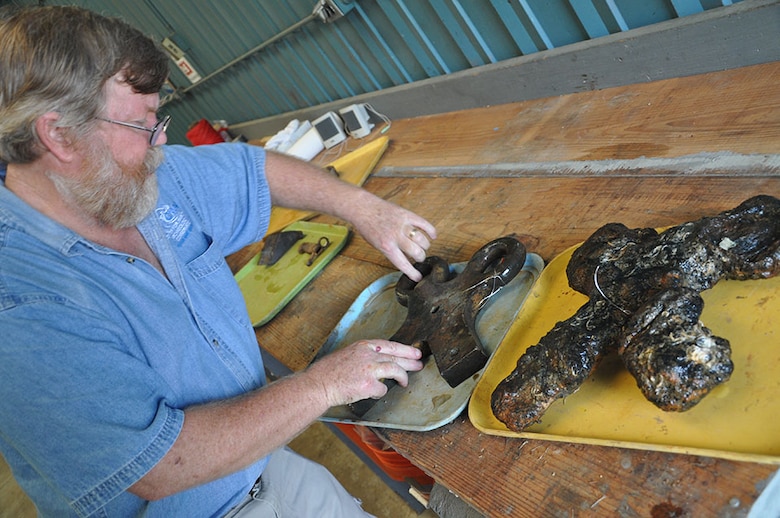Jim Jobling, a project manager with Texas A&M University’s Conservation Research Laboratory, positions two separate eyes for tackle from a pivot gun carriage. At left, a brass eye compared to an iron version of the same.