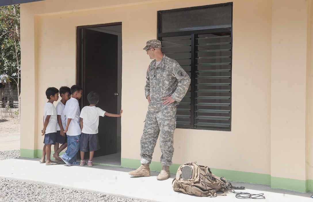 U.S. Army Spc. Edward Shipp, Detachment 1280, 324th Psychological Operations Company PSYOP specialist, watches as children peek into a new two-classroom building constructed by exercise Balikatan engineering teams during BK15’s San Rafael High School ribbon cutting ceremony, April 28, in San Rafael, Palawan, Philippines. Construction of the BK15 humanitarian civic assistance projects started this past March with the Armed Forces of the Philippines, U.S. forces and Australian forces working shoulder-to-shoulder to construct a two-classroom building for Santa Lourdes National High School, Sabang Elementary School, San Rafael High School and San Rafael Elementary School. This year marks the 31st iteration of the exercise, which is an annual Philippine-U.S. bilateral military training exercise and humanitarian civic assistance engagement. 