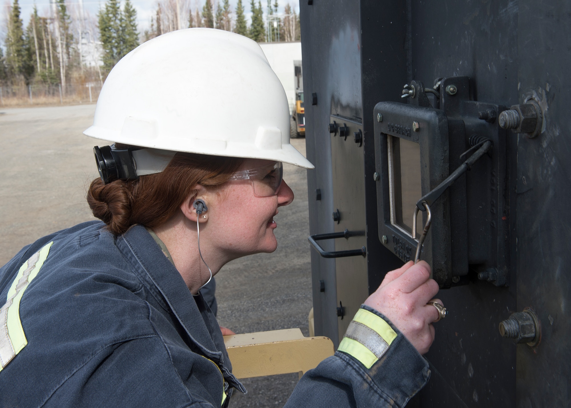 2nd Lt. Lindsey Mueller, 354th Logistics Readiness Squadron flight commander, looks through the window of a petroleum boiler at the flames that heat crude oil to more than 600 degrees while touring a local refinery in North Pole, Alaska, April 21, 2015. The refinery hosted the group to show how crude oil is processed into the JP-8 fuel the base uses for its missions. (U.S. Air Force photo by Staff Sgt. Shawn Nickel/Released)
