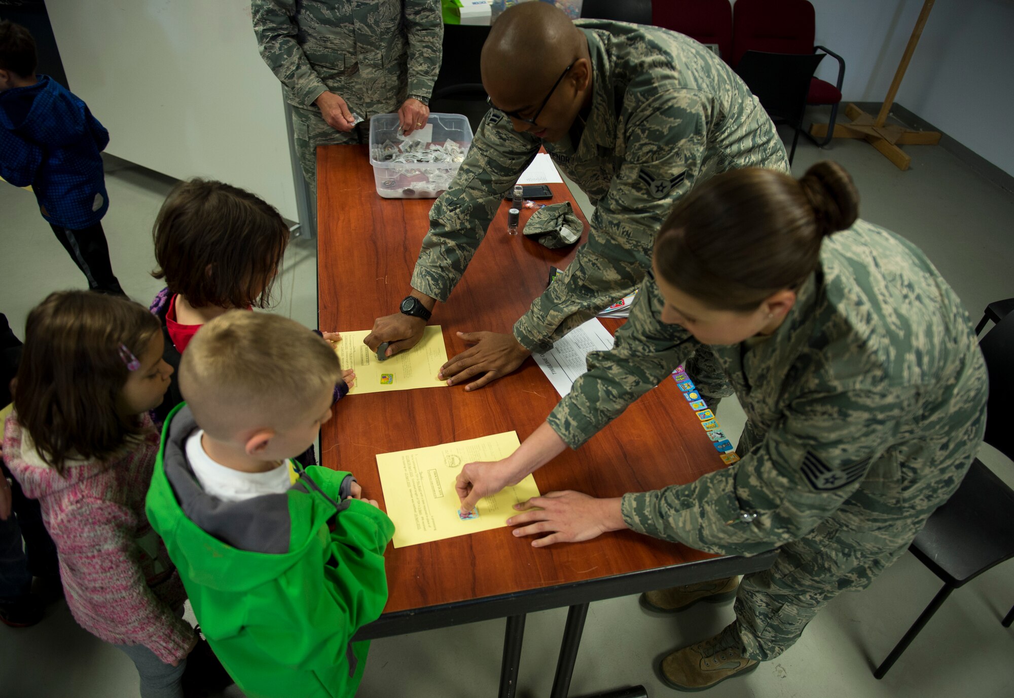 U.S. Air Force Airman 1st Class Vladimir Altenor and U.S. Air Force Staff Sgt. Katherine Solis, both 52nd Aerospace Medicine Squadron public health technicians, stamp orders and give out stickers during Kids’ Deployment Day at Spangdahlem Air Base, Germany, April 29, 2015. Altenor and Solis presented information on health issues the students might face on their simulated deployment to Rio De Janeiro. (U.S. Air Force photo by Airman 1st Class Luke Kitterman/Released)
