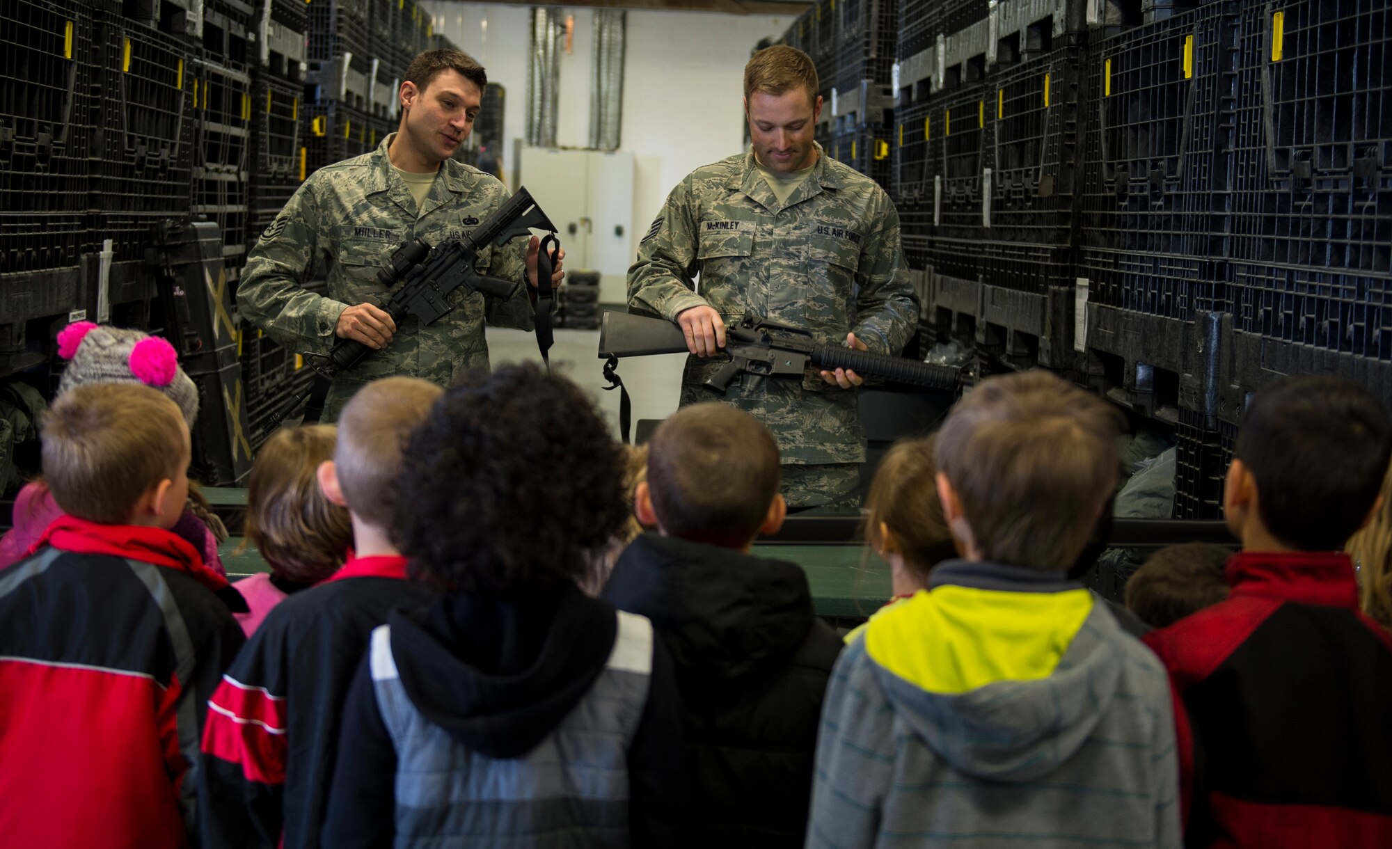 U.S. Air Force Staff Sgt. Shaun Miiller, left, and U.S. Air Force Staff Sgt. Kelley McKinley, both 52nd Logistic Readiness Squadron individual protective equipment supervisors, demonstrate weapon safety to students from Spangdahlem Elementary during Kids’ Deployment Day at Spangdahlem Air Base, Germany, April 29, 2015. The students learned about the different equipment Airmen need when deploying. (U.S. Air Force photo by Airman 1st Class Luke Kitterman/Released)