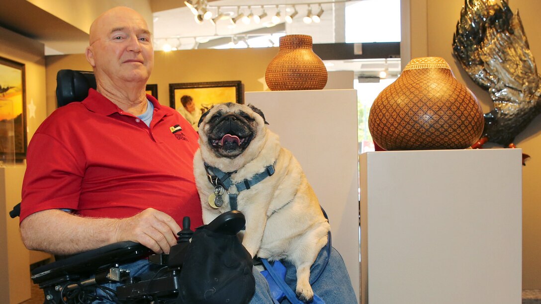 Jim Russell, a Marine veteran sits in the middle of the The Janice Griffiths Gallery at Marine Corps Base Camp Pendleton, California with his rotund service pug, Mr. Beau, resting on his lap July 24, 2015. The dim lights and cool interior of the gallery offer both some relief from the heat of the day as Russell recounts his tale of his life journey from military discipline to artistic expression. 