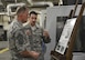 Staff Sgt. Nathaniel Ensing, 33rd Maintenance Squadron aircraft metals technician craftsman, explains the capability of the Ensing tool to Chief Master Sgt. of the Air Force James Cody his squadron’s coin at Eglin Air Force Base, Fla., July 30, 2015. The Ensing tool was named after Ensing who invented it to better assist in aligning parts within the F-35 Lightening II. (U.S. Air Force Photo/Senior Airman Andrea Posey)