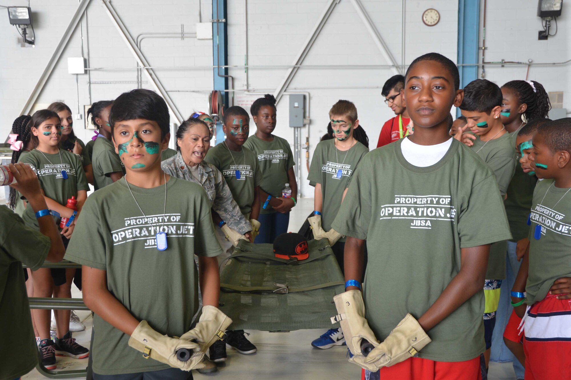 Maj. Julieta D. Benefield (left), a clinical nurse with the 433rd Medical Squadron, instructs children participating in Operation Junior Expeditionary Team event, learned how to carry a patient on a litter, July 31, 2015, on Joint Base San Antonio-Lackland, Texas. Children also learned how to apply pressure bandages and make slings for an injured arm. Learning first-hand what parents experience while deployed. (U.S. Air Force photo/Minnie Jones)