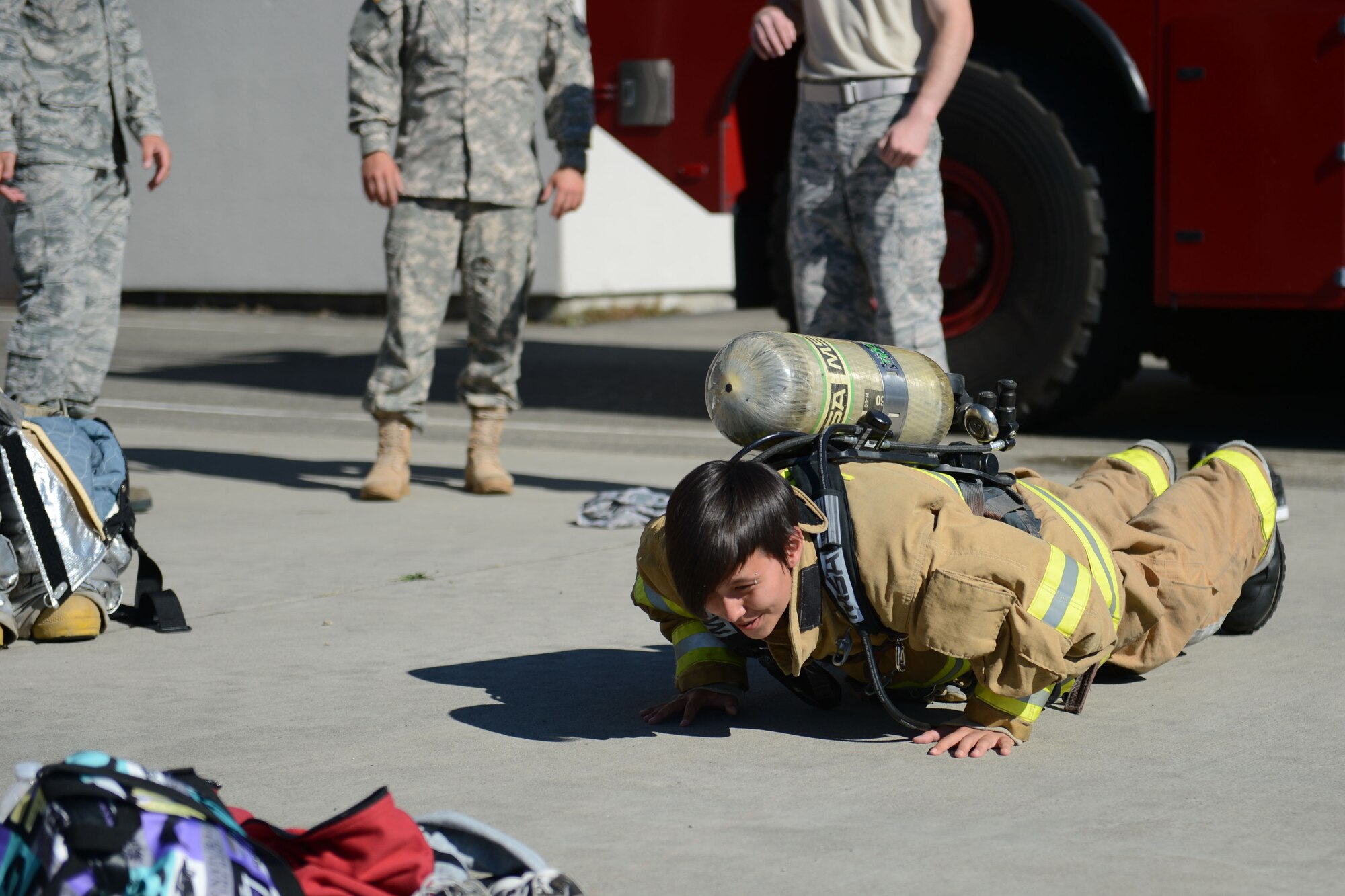 A member of the Nisqually Indian Tribe attempts a pushup while wearing firefighting gear and an oxygen tank during their tour of McChord Field, Wash., July 30, 2015. The tour, hosted by members of the McChord Field Top-3 organization, hosted more than 25 members of the Nisqually Indian Tribe from the Youth and Community Center. (U.S. Air Force photo/ Staff Sgt. Katie Jackson) 