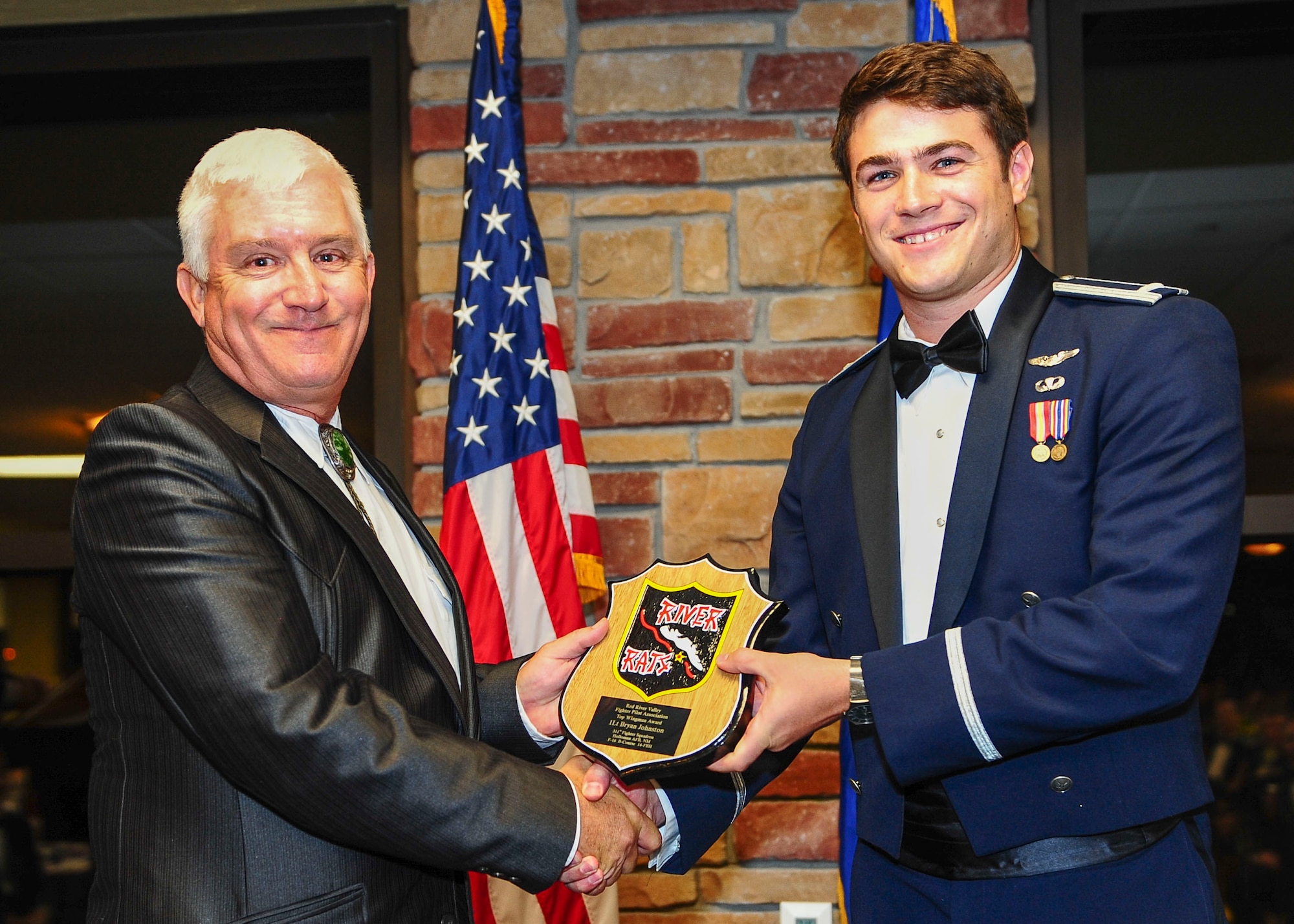 First Lt. Bryan Johnston (right) accepts the Red River Rat Award on July 31 at Holloman Air Force Base, N.M. as part of the 311th Fighter Squadron’s class 14-FBH graduation ceremony. The class is the first class of F-16 Fighting Falcon pilots to graduate from Holloman. The award was created by the Red River Valley Fighter Pilots Association. (U.S. Air Force photo by Amn Randahl J. Jenson)
