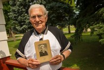 Lloyd Peterson, U.S. Navy World War II veteran, poses with a photo of himself from 1944 at his home in Carpio, N.D., July 10, 2015. Peterson served aboard the USS Southampton from 1944 to 1946. (U.S. Air Force photo/Senior Airman Apryl Hall)
