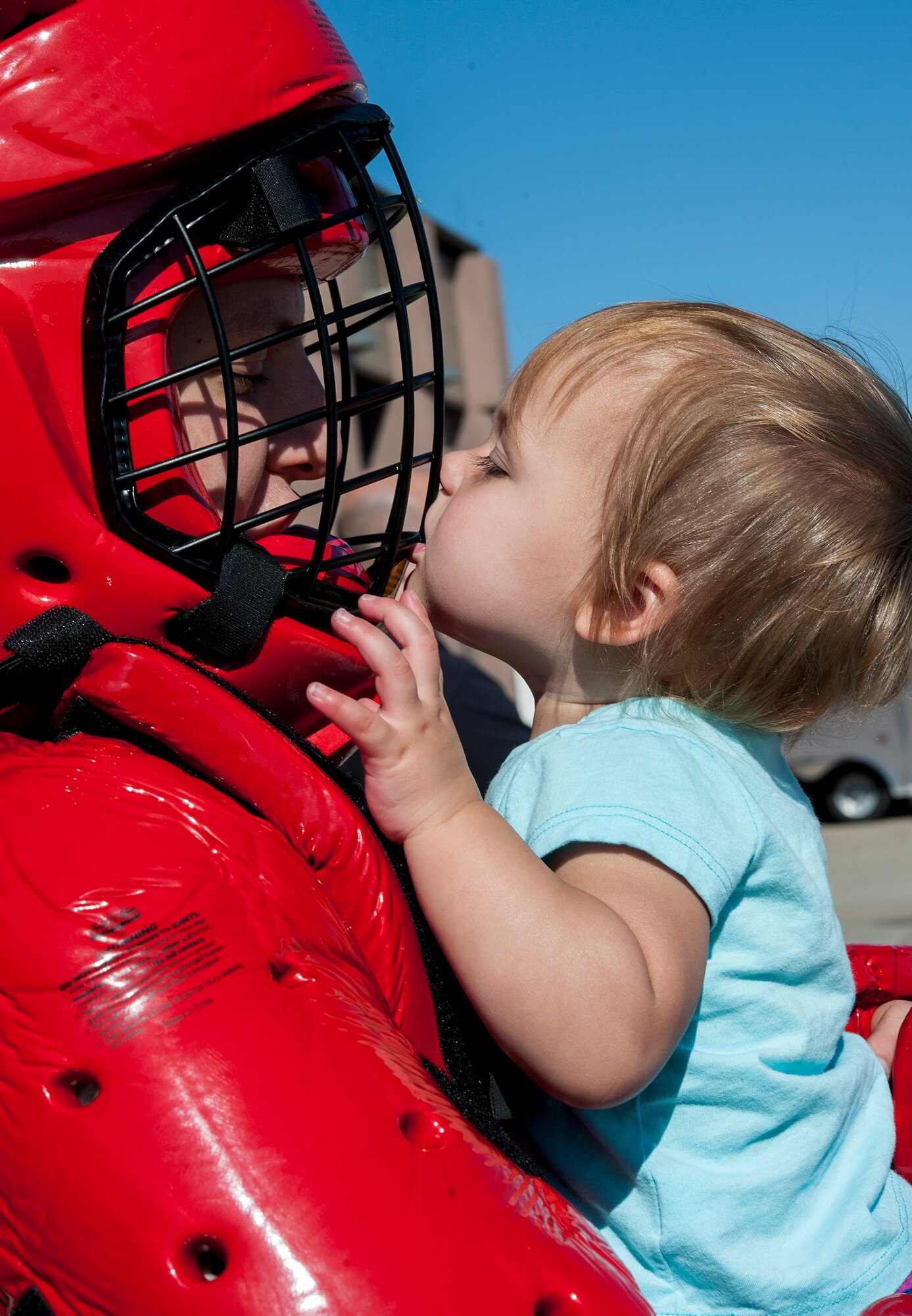 Staff Sgt. Justin McCoy, 5th Security Forces Squadron armory assistant NCO in charge, receives a kiss from his daughter Tateleigh during the Hero in Training event at Minot Air Force Base, N.D., July 31, 2015. McCoy wore a "red man" suit, which is commonly used by the squadron during baton and combative training, and allowed base children to practice with the baton on the suit. (U.S. Air Force photo/Senior Airman Stephanie Morris)