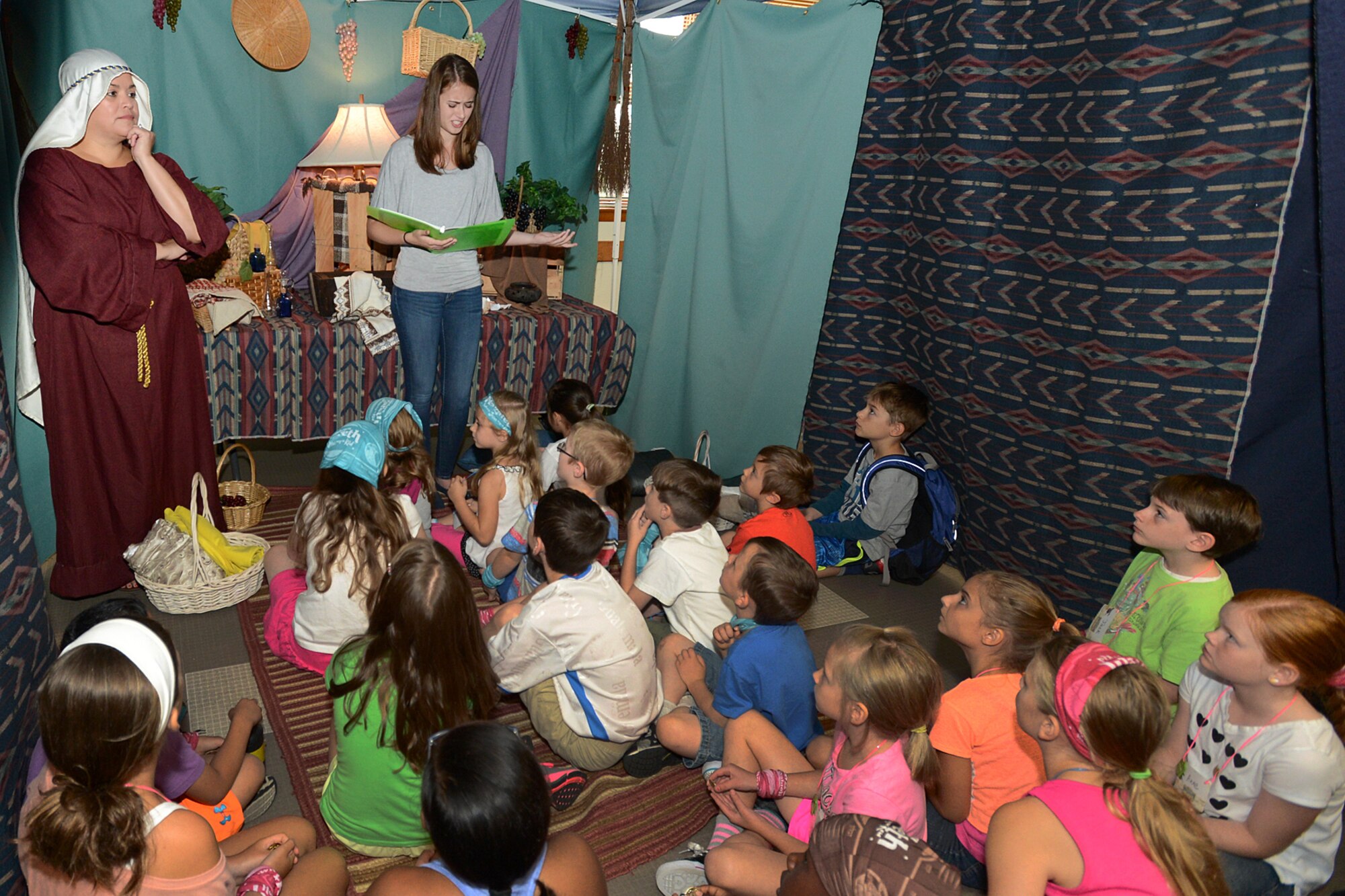 Mary Garcia, left, and Jillian Boersma, both volunteers, speak to children about what life was like for children in biblical times during Vacation Bible School at the base chapel Aug. 4. This year’s VBS has nearly 100 children ages 5 through sixth grade participating. (U.S. Air Force photo by Jerry Saslav)