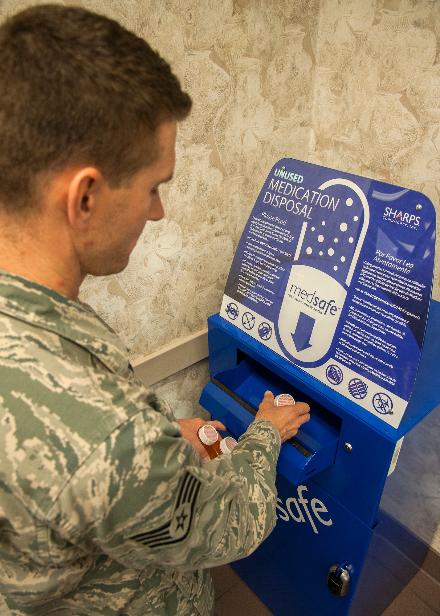 An Airman drops medicine in the Satellite Pharmacy's new MEDSAFE unit. Patients can now deposit all medications, to include creams, liquids and unused medical emergency pens in the blue steel bin located in the corner of the lobby by the prescription pick-up window. (U.S. Air Force photo/Ilka Cole)