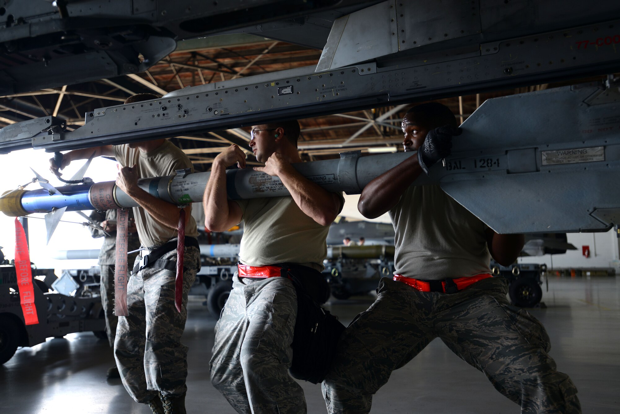 U.S. Air Force Airmen from the 20th Aircraft Maintenance Squadron, 77th Aircraft Maintenance Unit, work together to load munitions onto the wing of an F-16CM Fighting Falcon during a weapons load crew of the quarter competition at Shaw Air Force Base, S.C., July 31, 2015. Pitted against the 79th AMU, the 77th AMU raced to determine which unit could safely and accurately load munitions the fastest. (U.S. Air Force photo by Airman 1st Class Kelsey Tucker/Released)
