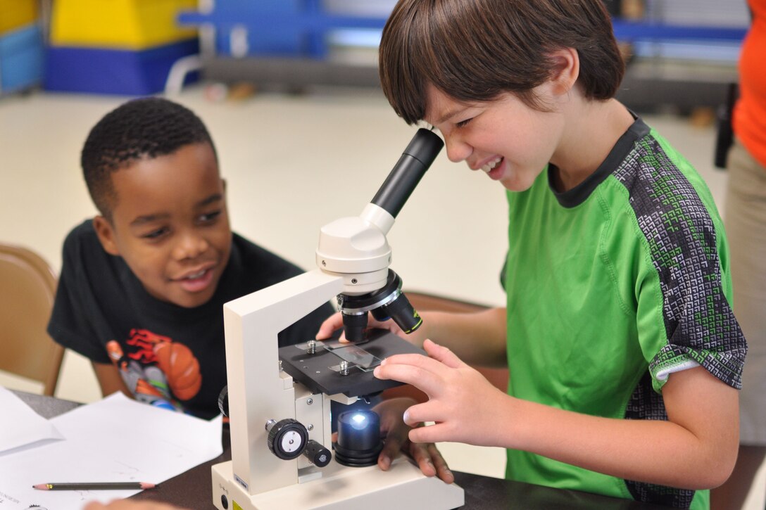 Marcus, age 10 and Nathanael, age 9, share a microscope to view hair fibers in a Crime Scene Investigation workshop July 28 at The Quantico Youth Center. The boys learn how the collection of hair and fiber help a forensic scientist solve a crime.