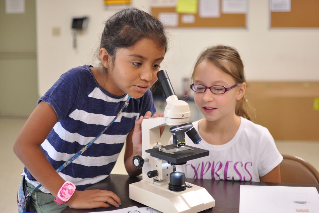 Sofia, age 10, and Lael, age 11, take turns looking at hair fibers under a microscope in a Crime Scene Investigation workshop July 28 at The Quantico Youth Center. The girls learned to use cutting edge technology to analyze and record data.
