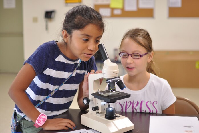 Sofia, age 10, and Lael, age 11, take turns looking at hair fibers under a microscope in a Crime Scene Investigation workshop July 28 at The Quantico Youth Center. The girls learned to use cutting edge technology to analyze and record data.