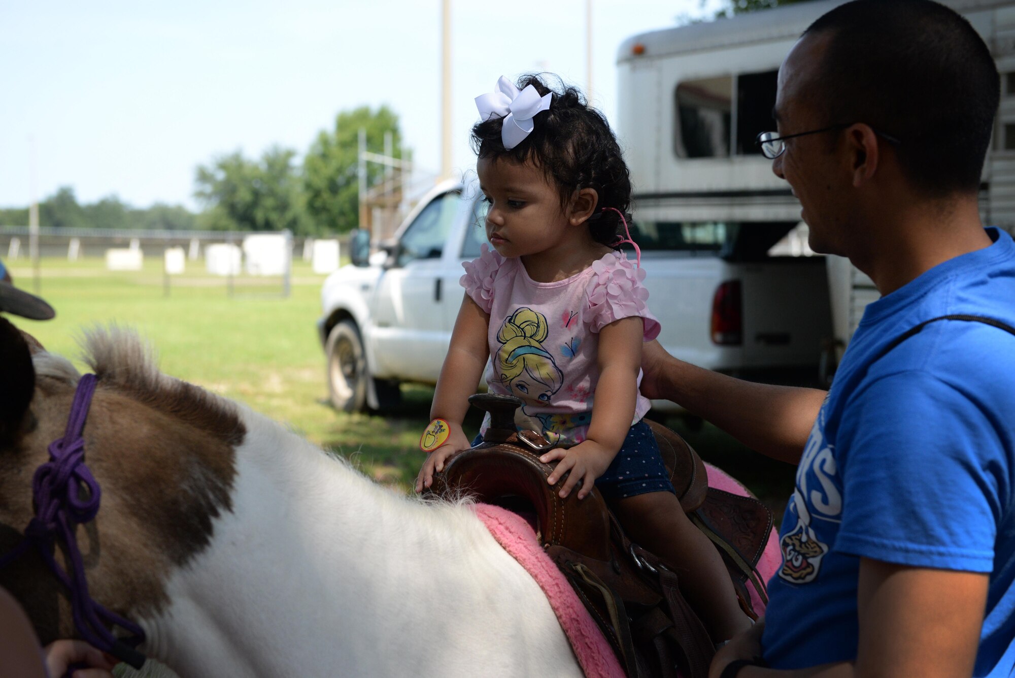 Ariana Rose Camacho rides a pony with the help of her dad Capt. Santiago Camacho, 335th Training Squadron force support training flight commander, at the Exceptional Family Member Program Information and Resource Fair, Aug. 1, 2015, Keesler Air Force Base, Miss. EFMP, with help from Keesler Integrated Resource Team organizations, provided carnival games, hands-on activities and information about support programs to families with special needs dependents. (U.S. Air Force photo by Senior Airman Holly Mansfield)
