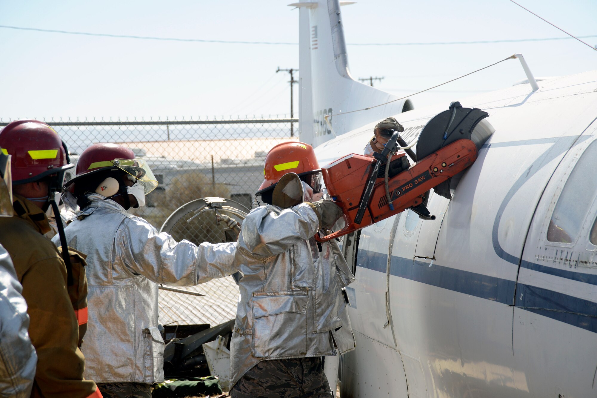 One firefighter supports another as the rescue saw reaches the top of the plane. (Air Force photo by Patric Lovato)