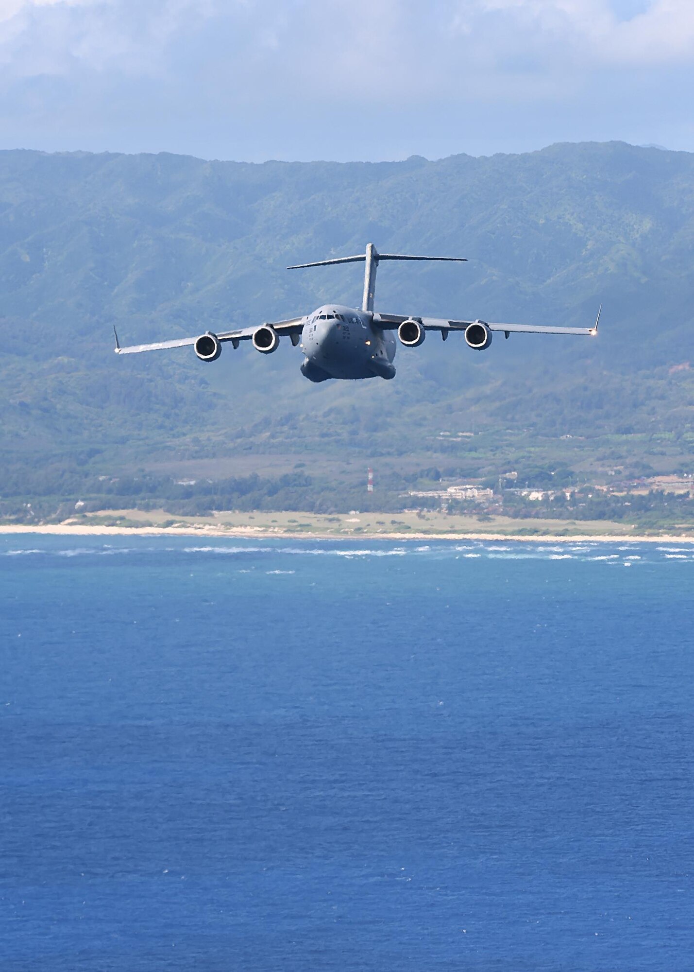 A C-17 Globemaster III from the 535th Airlift Squadron flies over the north shore of the island of Oahu, Hawaii, July 31, 2015. Air Force active duty and Air National Guard Airmen joined forces in a Warrior Day to demonstrate the cooperation and capabilities of total force integration. Training simulations included combat maneuvers in a hostile environment, air drops, and refueling operations. It also included an engine- running crew change of three of the C-17s. (U.S. Air Force photo by Tech. Sgt. Aaron Oelrich/Released)