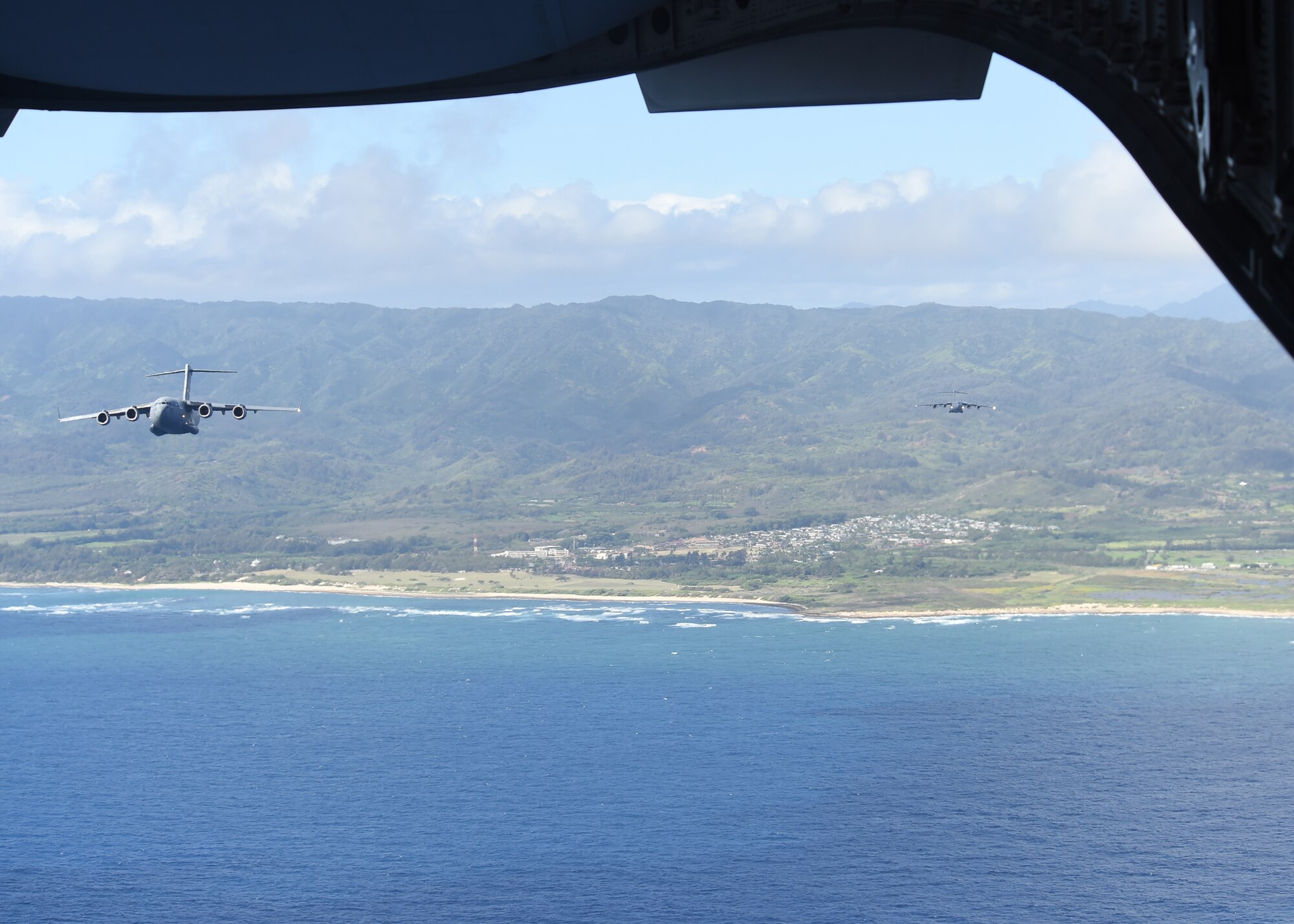 Two C-17s from the 535th Airlift Squadron fly in formation over the north shore of the island of Oahu, Hawaii, July 31, 2015. Air Force active duty and Air National Guard Airmen joined forces in a Warrior Day to demonstrate the cooperation and capabilities of total force integration. Training simulations included combat maneuvers in a hostile environment, air drops, and refueling operations. It also included an engine-running crew change of three of the C-17s. (U.S. Air Force photo by Tech. Sgt. Aaron Oelrich/Released))