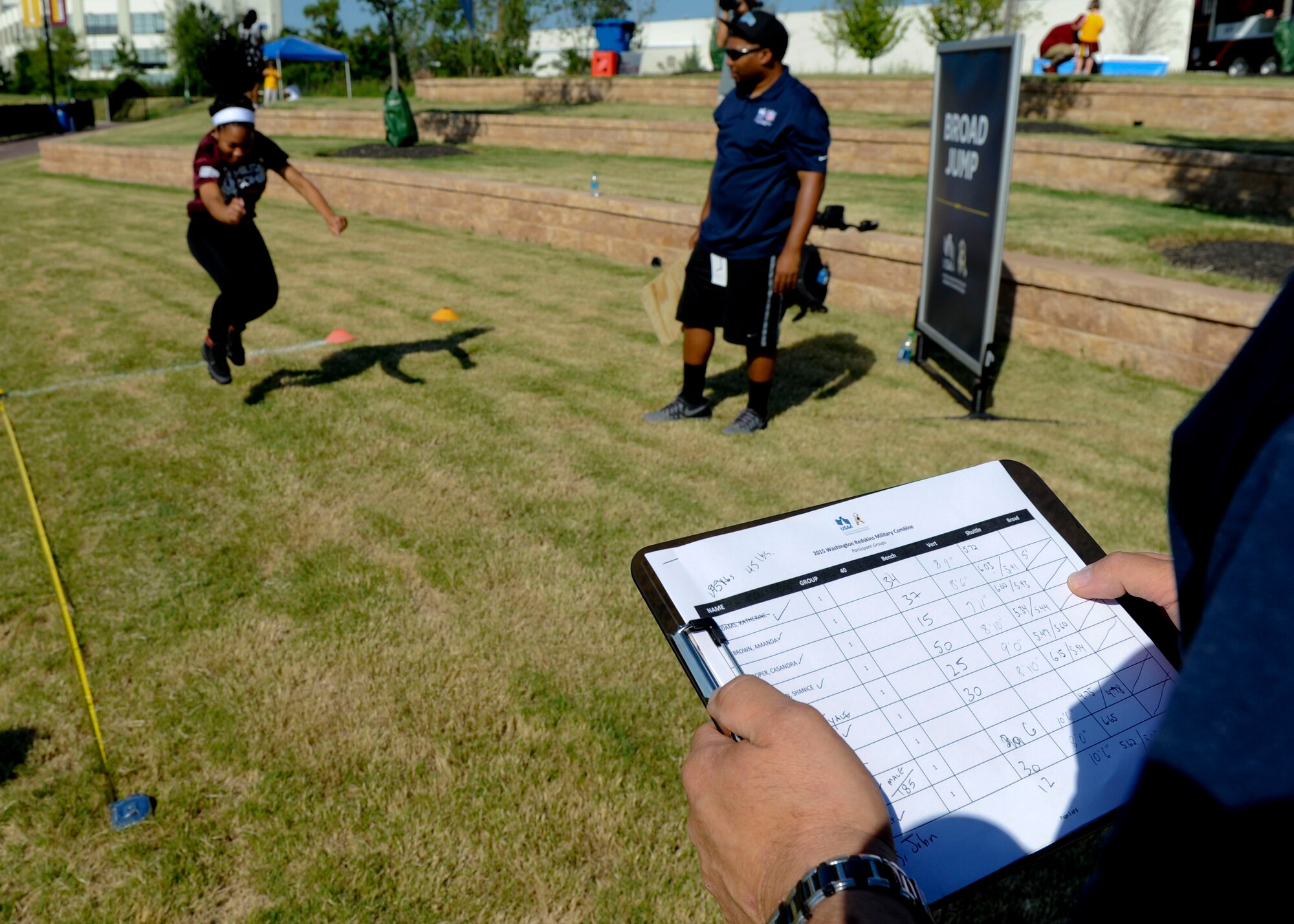 U.S. Navy Aviation Maintenance Administration Second Class Casandra Cooper, performs a broad jump while coaches observe during the USAA and Washington Redskins Military Combine at the Bon Secours Training Center in Richmond, Va., July 31, 2015. The combine consisted of five events: bench-press, 20-yard shuttle, vertical leap, broad jump and a 40-yard dash. (U.S. Air Force photo by Staff Sgt. John D. Strong II/Released)