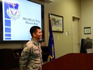 Staff Sgt. Guerddy Espinoza, First Term Airman Center NCO in charge, observes his class during a mission orientation briefing July 17, 2015, at Malmstrom Air Force Base, Mont. Espinoza usually assists the base commander or vice commander with these briefings by clicking through the slideshow presentation. (U.S. Air Force photo/Airman 1st Class Magen M. Reeves)