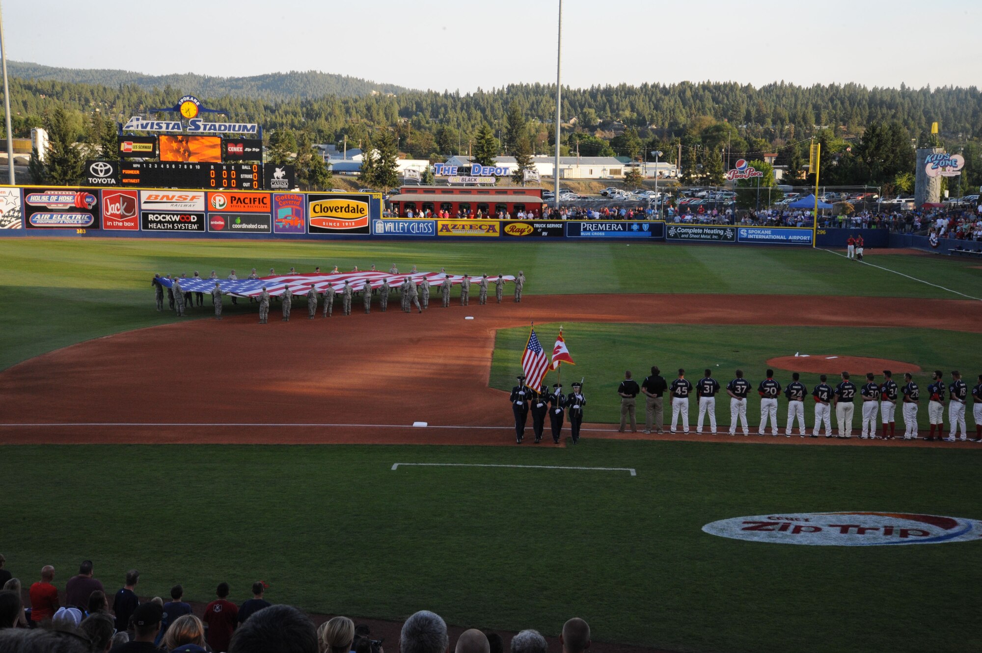 Members of the 141st Air Refueling Wing Honor Guard march off the field following the singing of the National Anthem while Fairchild Airmen unfurl the big flag at Avista Stadium in Spokane, Wash., Aug. 4, 2015. The 141st ARW honor guard worked in conjunction with the Team Fairchild flag holders to open events at the Short Season Single A baseball All-Star game. (U.S. Air Force photo/Senior Airman Sam Fogleman)