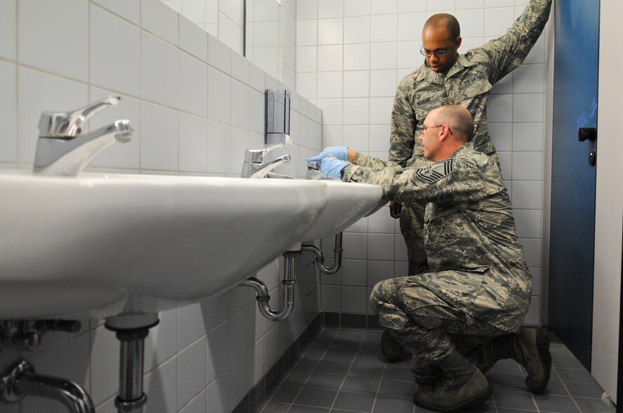 U.S. Air Force Chief Master Sgt. Wayne Miller, New Jersey Air National Guard's 177th Medical Group superintendent, collects a water sample from the bathroom of a school in Bitburg, Germany, as Master Sgt. Julius Simmons observes, Aug. 5. The school is a Department of Defense Dependents School for military members on Spangdahlem Air Base. (U.S. Air National Guard photo by Senior Airman Shane S. Karp/Released)