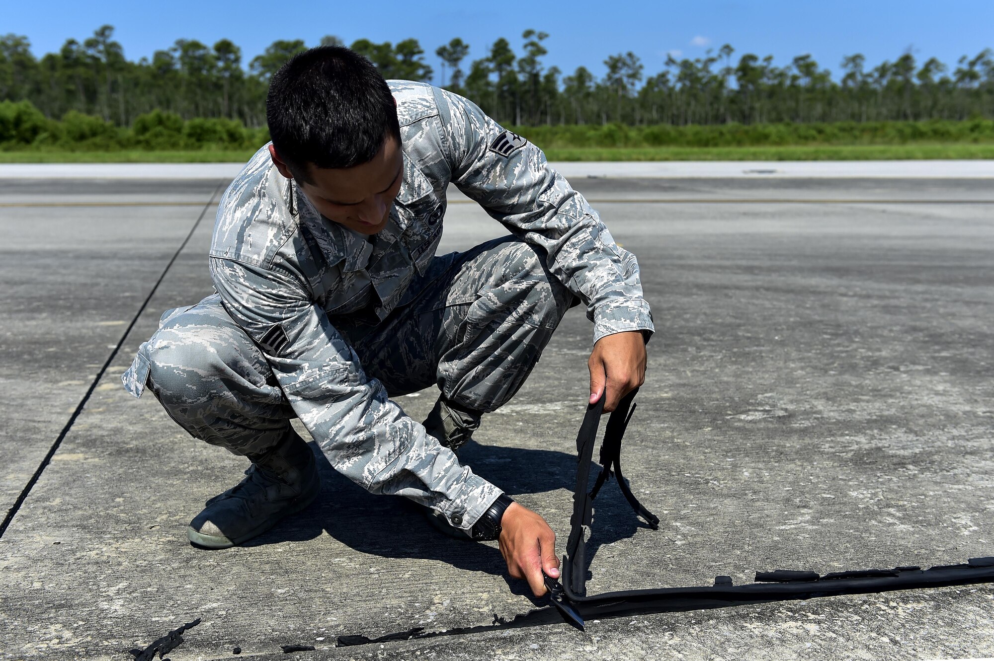 Senior Airman David Rios, 1st Special Operations Support Squadron airfield management operations shift leader, removes excess pavement sealant during an airfield check on Hurlburt Field, Fla., Aug. 4, 2015. Routine airfield checks are performed to check and maintain the airfield to prevent any mishaps during aircraft movement. (U.S. Air Force photo/Senior Airman Jeff Parkinson)