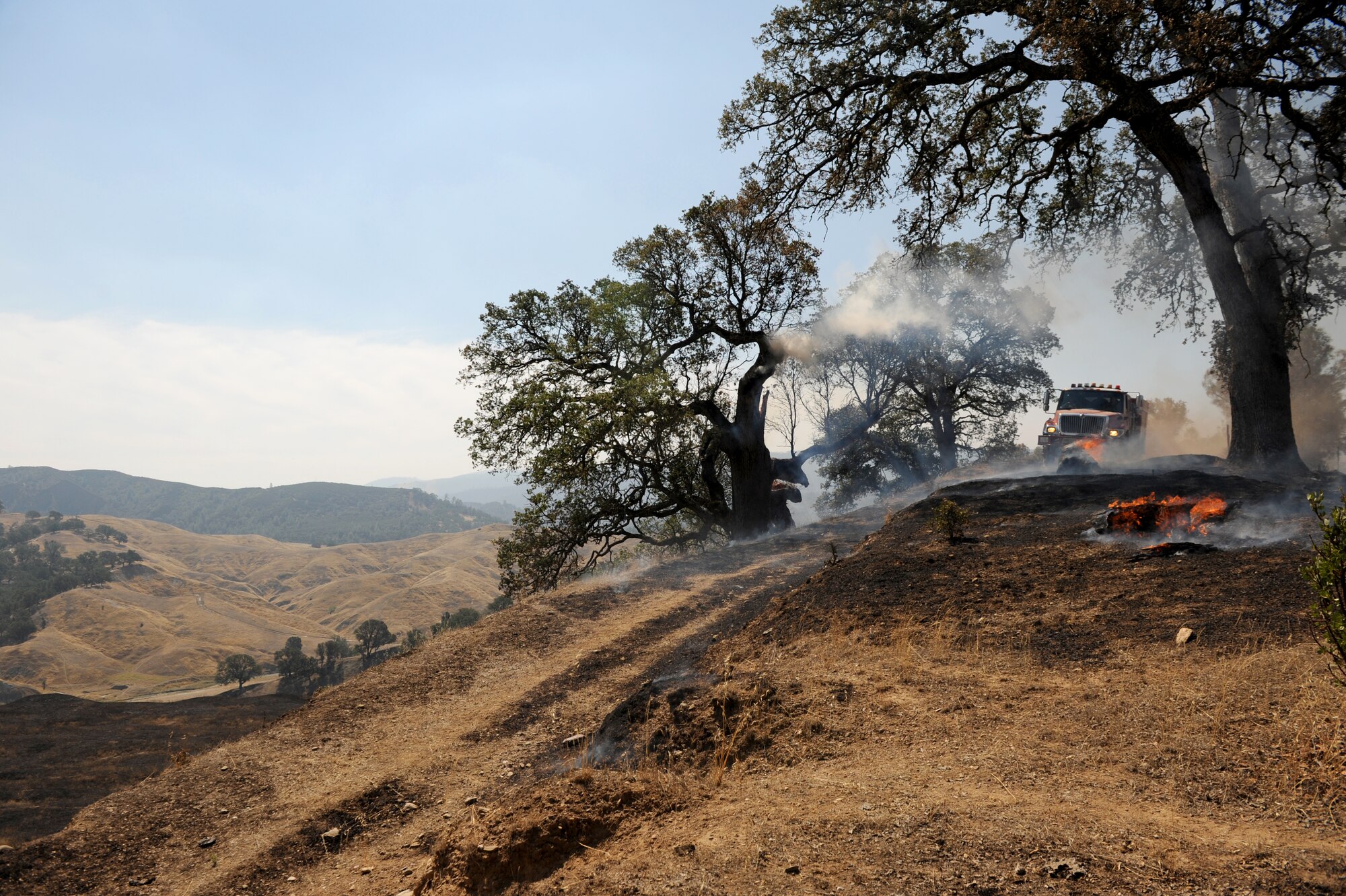A fire engine operator drives up a road behind a burning fire, Aug. 6, 2015, near Clearlake, California. The Rocky Wildfire has consumed nearly 70,000 acres in Northern California. (U.S. Air Force Photo by Airman Preston L. Cherry)